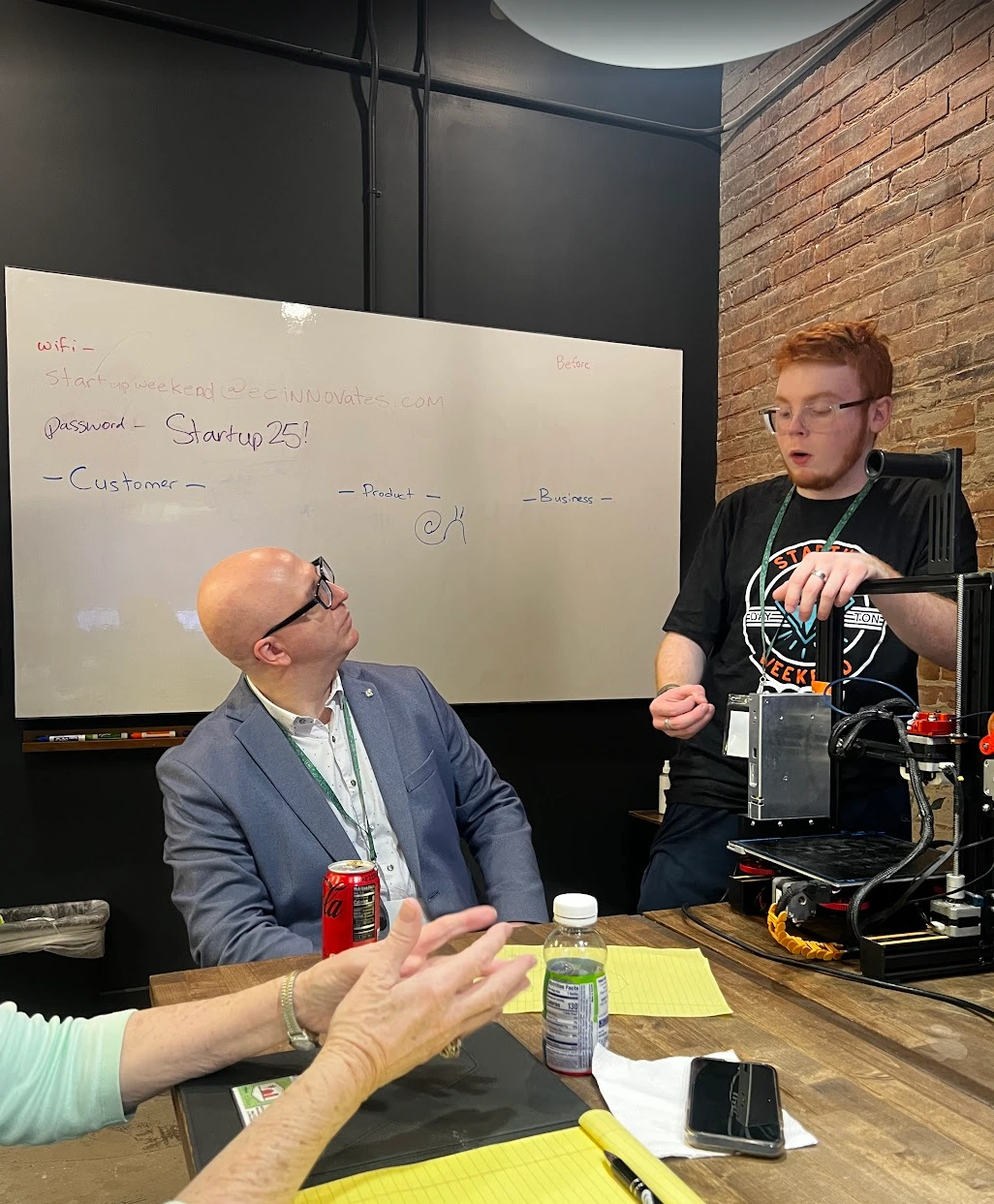 Two team members discussing a prototype beside a 3D printer.